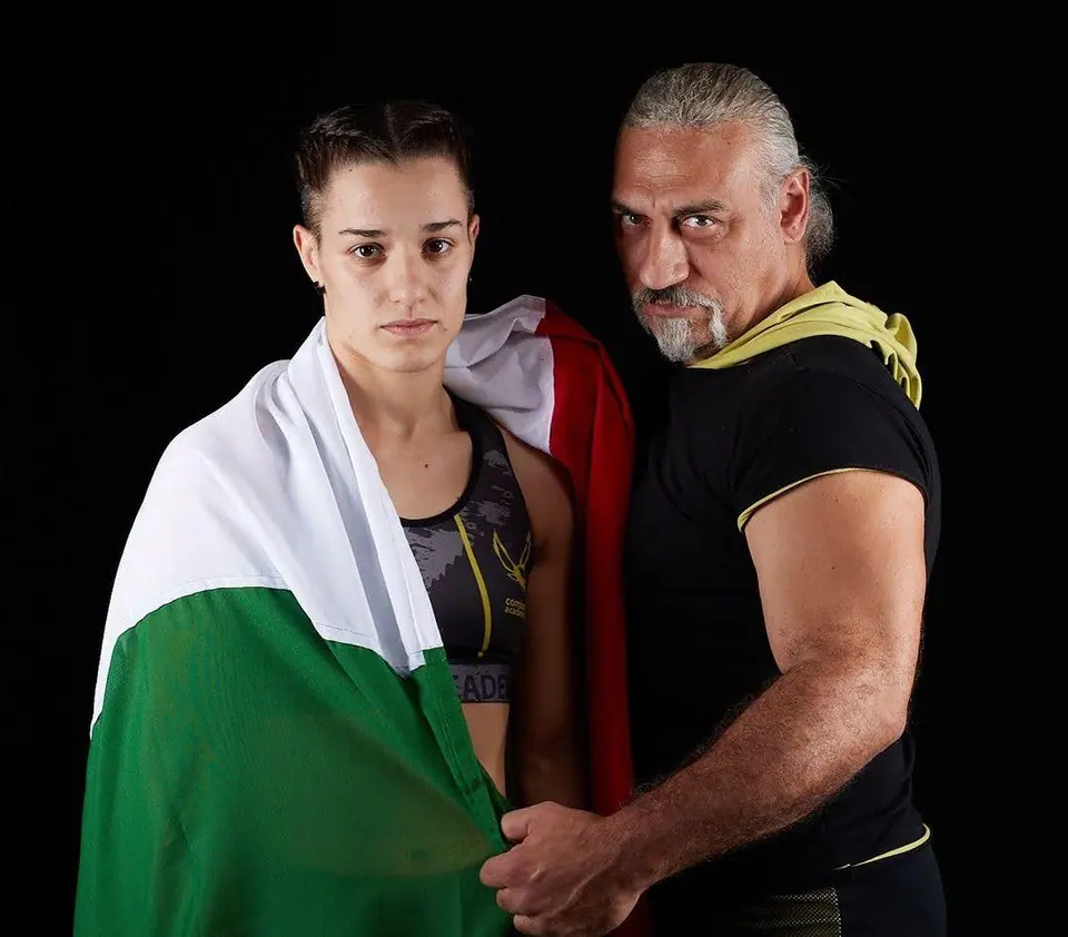 Il Maestro Simone Palazzin accanto a un’atleta della scuola avvolta nel tricolore, ritratto su fondo nero