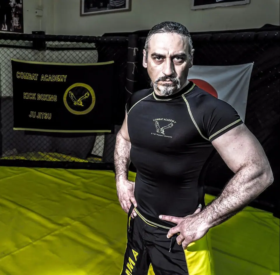 Il Maestro Simone Palazzin in posa nella gabbia, davanti al telo con l’aquila Combat Academy