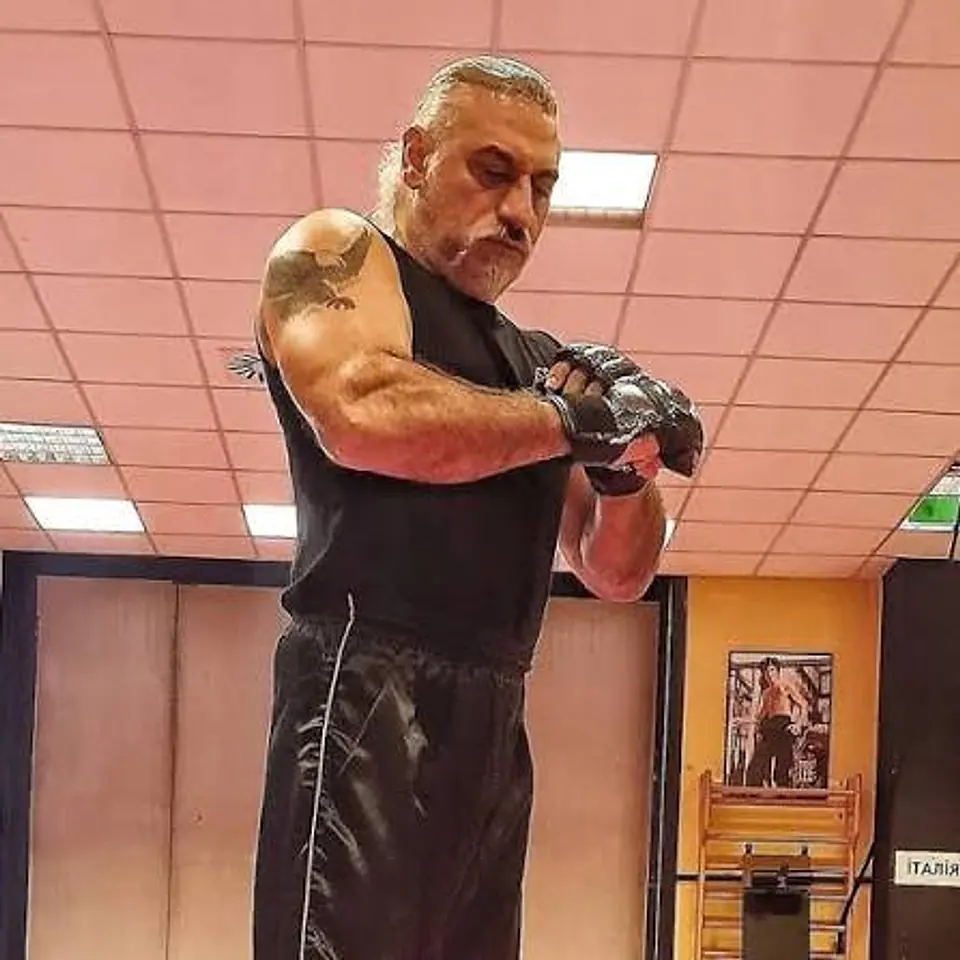 Il Maestro in palestra si sistema i guantini da MMA; sul braccio il tatuaggio di un’aquila